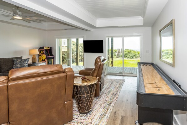 A modern living room with a pool table, leather sofas, a drum, and a television. - Renovated ocean-view home with beachfront access, hot tub, pool table, & deck (North Topsail Beach)