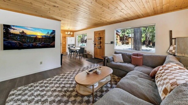 A modern living room with a wooden ceiling, a large painting, a sofa, and a dining area.