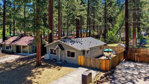 A single-story house with a sloped roof, surrounded by tall pine trees, in a wooded area.