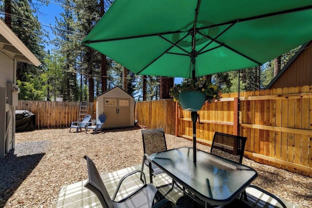 Une terrasse extérieure avec une table et des chaises, un parasol vert et une clôture en bois.