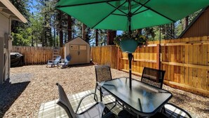 An outdoor patio with a table and chairs, a green umbrella, and a wooden fence.