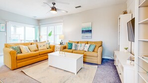 A living room with two sofas, a coffee table, a TV, and a ceiling fan. - Incredible waterfront condo with amazing ocean views, pool, deck, & beach access (Avon)
