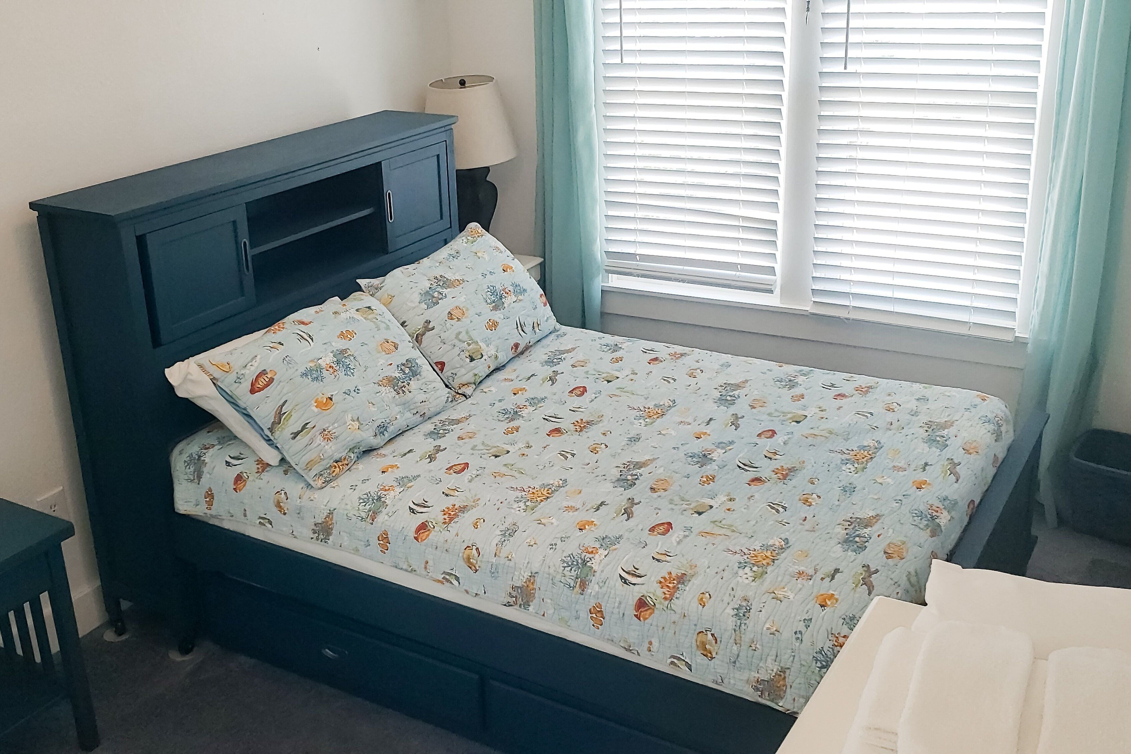 A bedroom with a bed, a nightstand, a lamp, and a window with blinds.