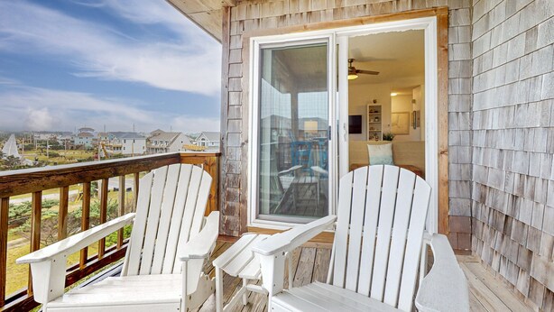 A wooden deck with two white Adirondack chairs and a glass door leading to an interior space. - Incredible waterfront condo with amazing ocean views, pool, deck, & beach access (Avon)