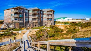A multi-story building with balconies, a wooden deck, and a beach view. - Incredible waterfront condo with amazing ocean views, pool, deck, & beach access (Avon)