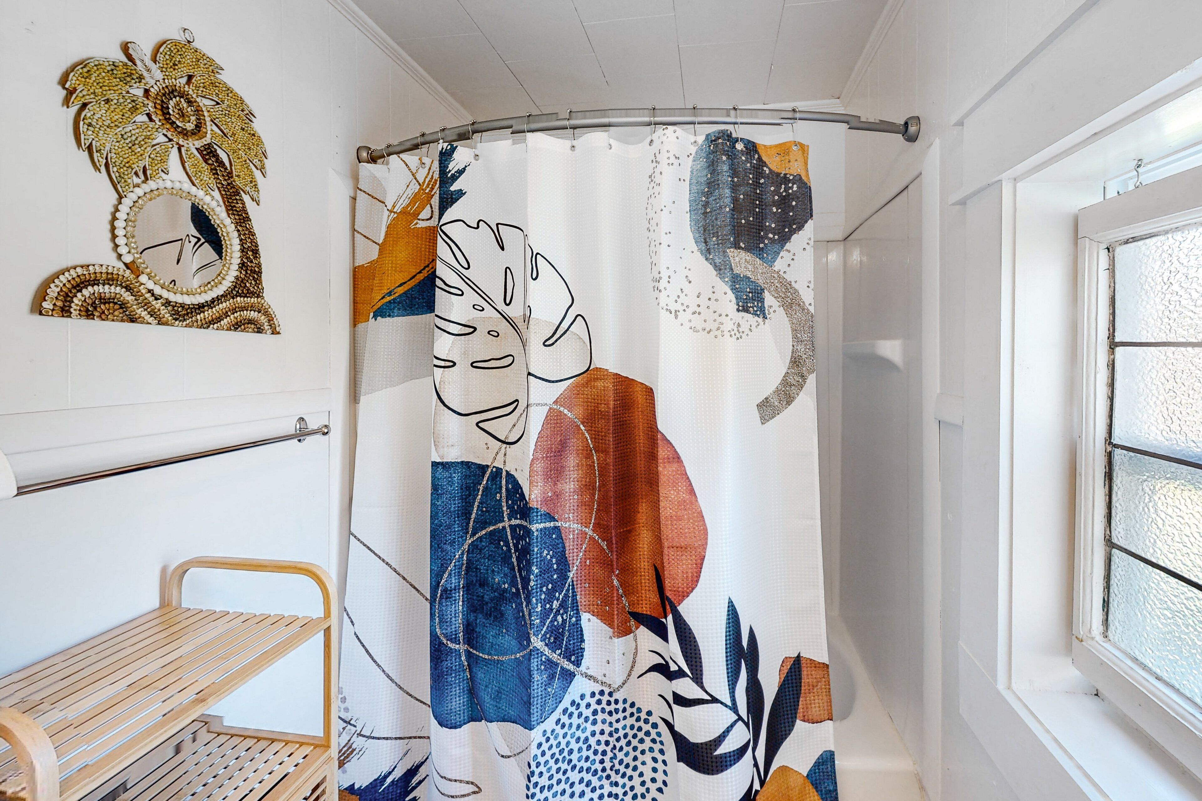En duschdraperi med ett blommönster, en träbänk och en väggmonterad spegel med en dekorativ design.