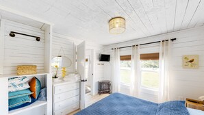 Ein Schlafzimmer mit einem großen Bett, einem Schminktisch, einem Fernseher und einem Fenster mit Vorhängen.