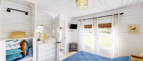 Um quarto com uma cama grande, cômoda, televisão e janela com cortinas.