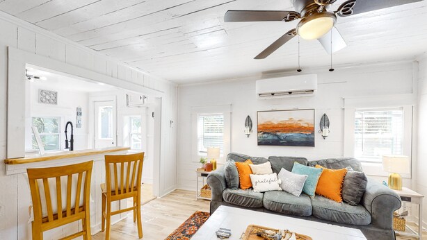 Ein geräumiges Wohnzimmer mit grauem Sofa, Holzstühlen, einem weißen Couchtisch und einem Deckenventilator.