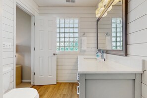 A bathroom with a white door, a window with a grid pattern, a sink, and a mirror. - Putt & Paddle Paradise: Canalfront, putting green (Ocean Isle Beach)