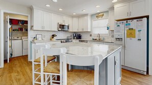 Cocina moderna con armarios blancos, una isla central con taburetes y electrodomésticos integrados, además de un refrigerador con imanes.