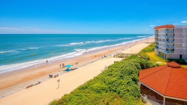 Ein Hotel direkt am Strand mit einem Gebäude mit rotem Dach, Sandstrand und dem Meer.