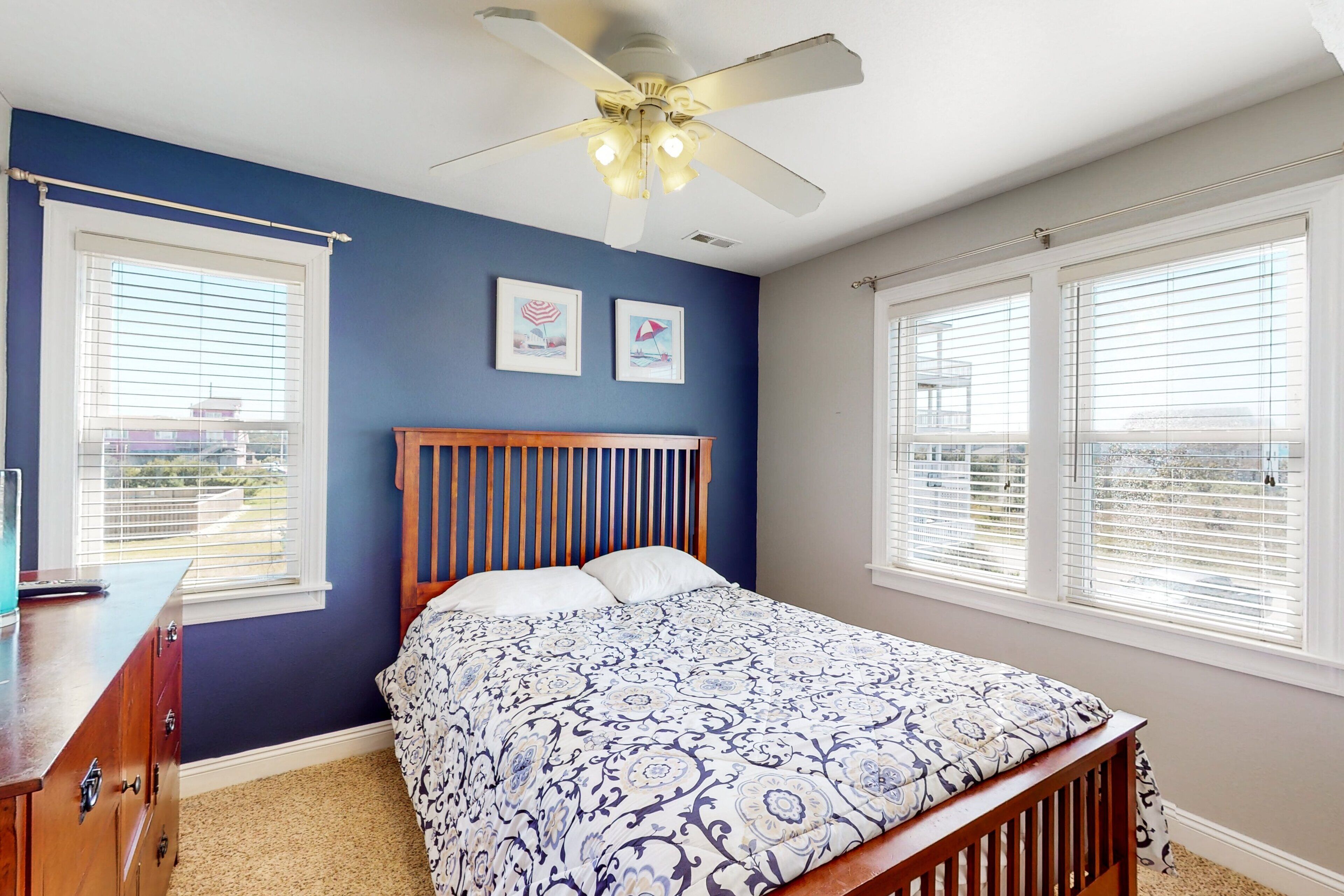 A bedroom with a bed, a wooden headboard, a ceiling fan, and two windows with blinds.