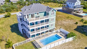 A multi-story house with a swimming pool, surrounded by a white fence.