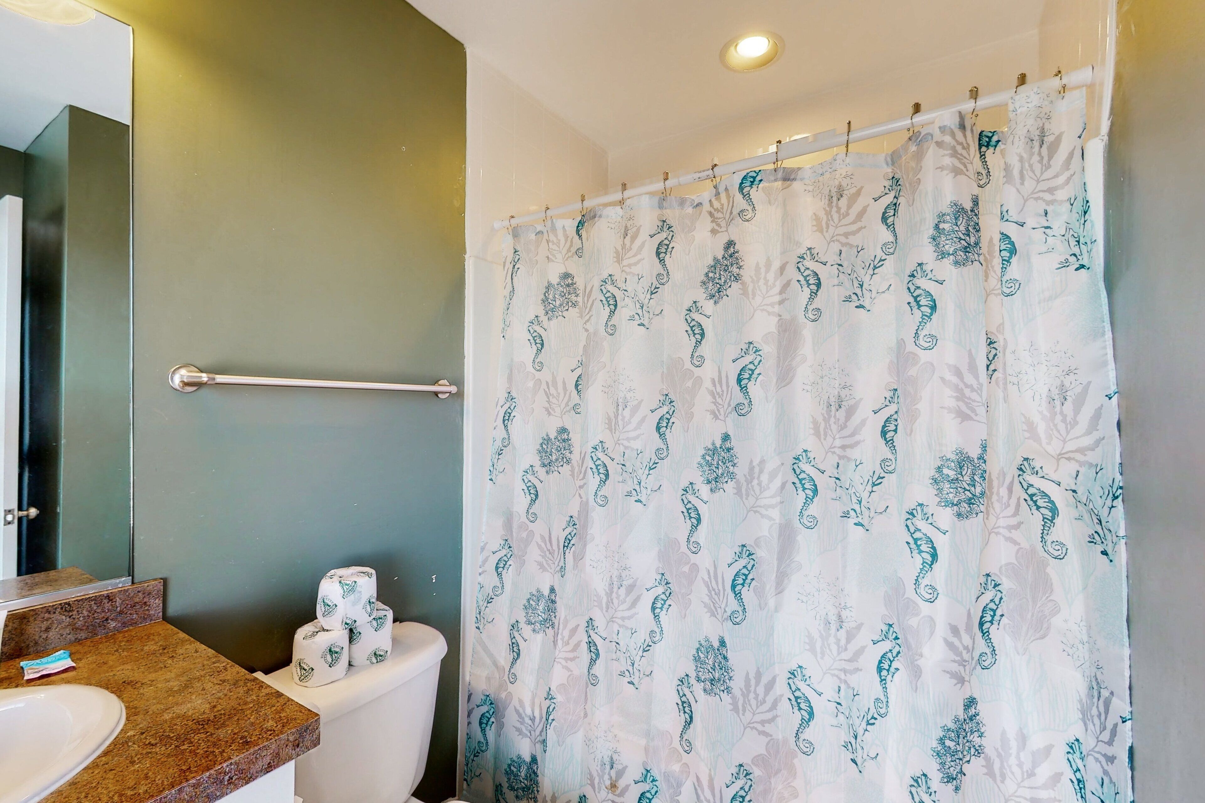 Un baño con inodoro, lavamanos, toallero y cortina de ducha con estampado de caballito de mar.
