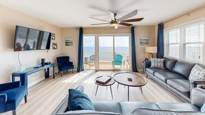 A living room with a TV, sofa, coffee table, and a balcony with outdoor furniture. - Renovated townhome right on the ocean with private beach & coffee stations (North Topsail Beach)
