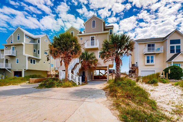 A beachfront residential area with multi-story houses, a paved driveway, and palm trees.