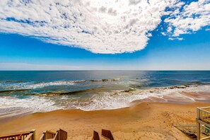 A beach with a wooden walkway leading to the ocean, clear skies, and waves crashing onto the shore.