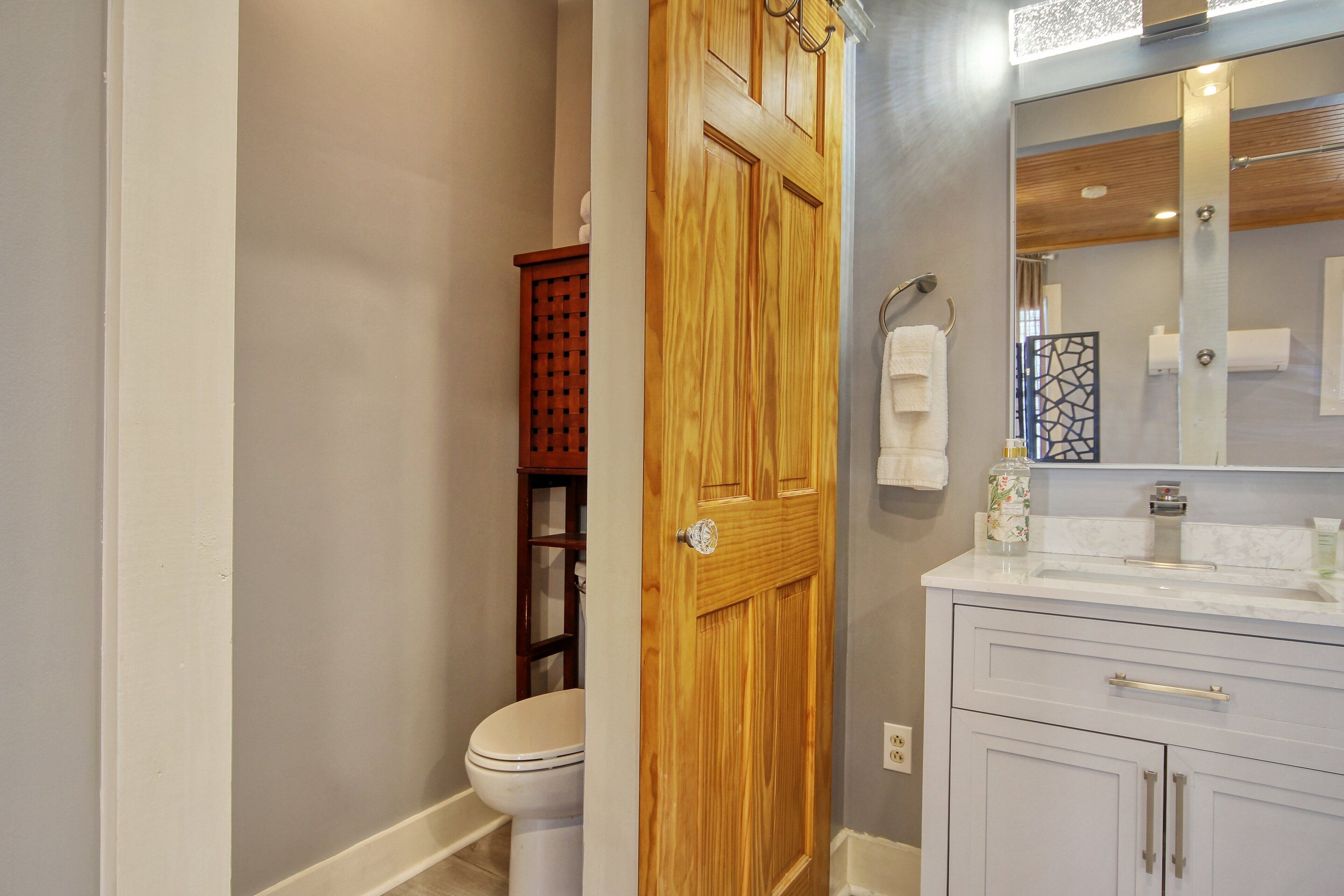 A bathroom with a wooden door, a toilet, a vanity with a mirror, and a towel rack.