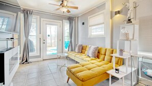 Un salon moderne avec un canapé jaune, un ventilateur de plafond et une table basse en verre.