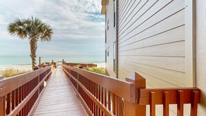 A wooden walkway leading to a beach, with a palm tree and ocean view. - Charming ocean-view condo with washer/dryer, on-site pool (North Topsail Beach)