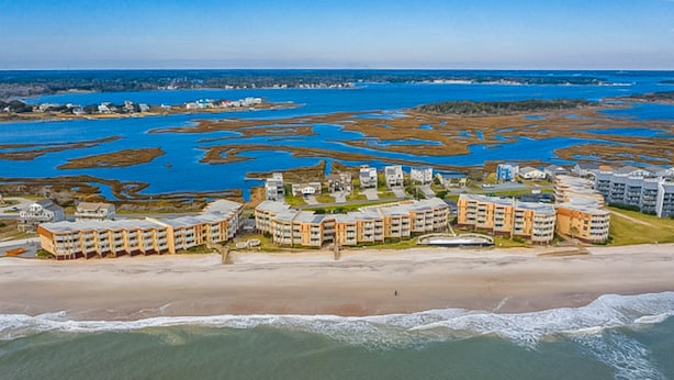 A coastal hotel with multiple buildings, a beach, and a marshy area in the background. - Charming ocean-view condo with washer/dryer, on-site pool (North Topsail Beach)