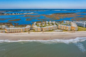 A coastal hotel with multiple buildings, a beach, and a marshy area in the background.