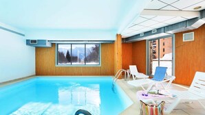 Una piscina interior con ventanas amplias, sillones de descanso y vistas a montañas.