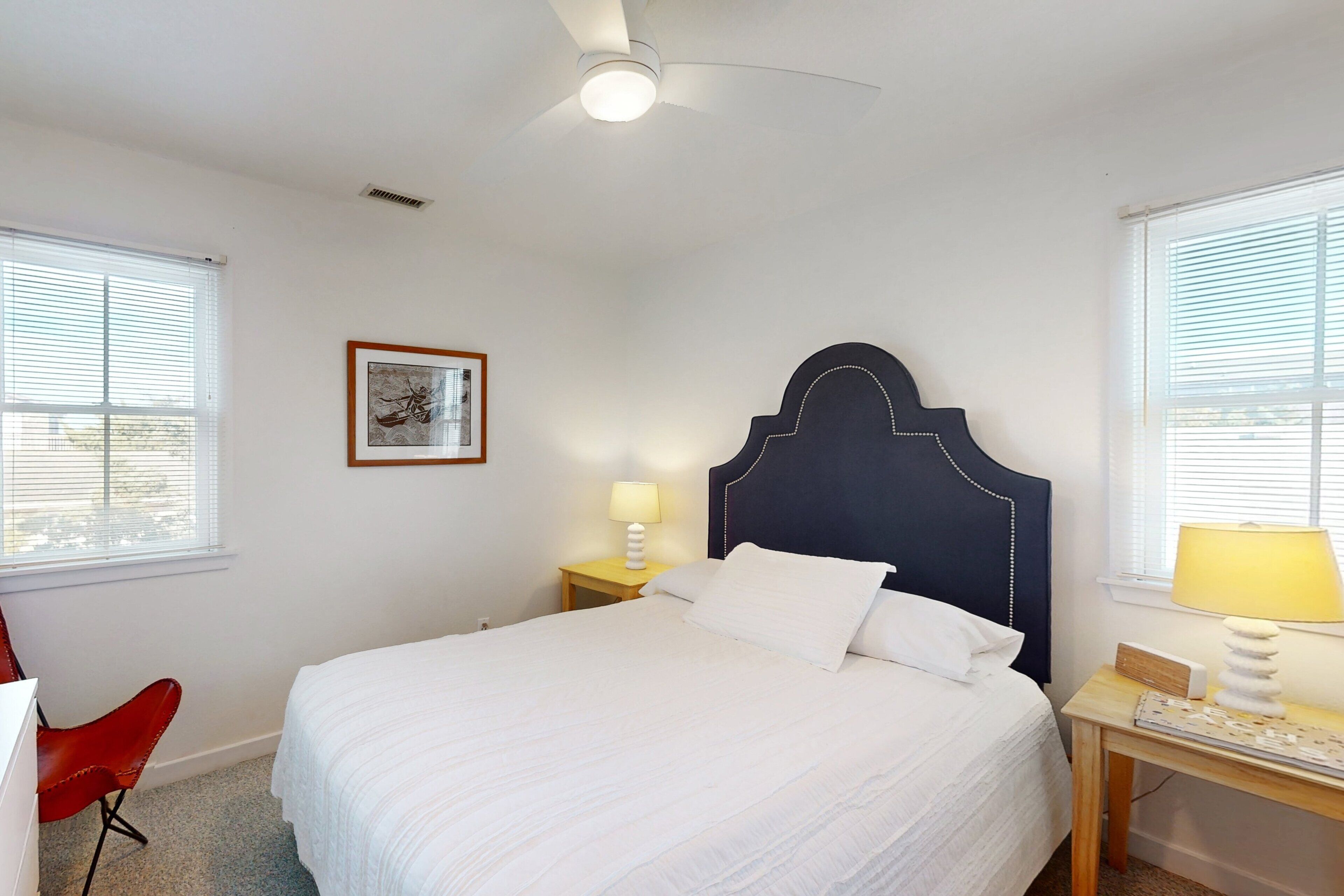 Une chambre à coucher avec un lit, une table de chevet, une chaise et un ventilateur de plafond.