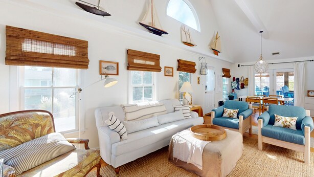 Ein geräumiges Wohnzimmer mit hohen Decken, großen Fenstern und maritimer Dekoration, darunter Schiffmodelle und ein Segelboot.