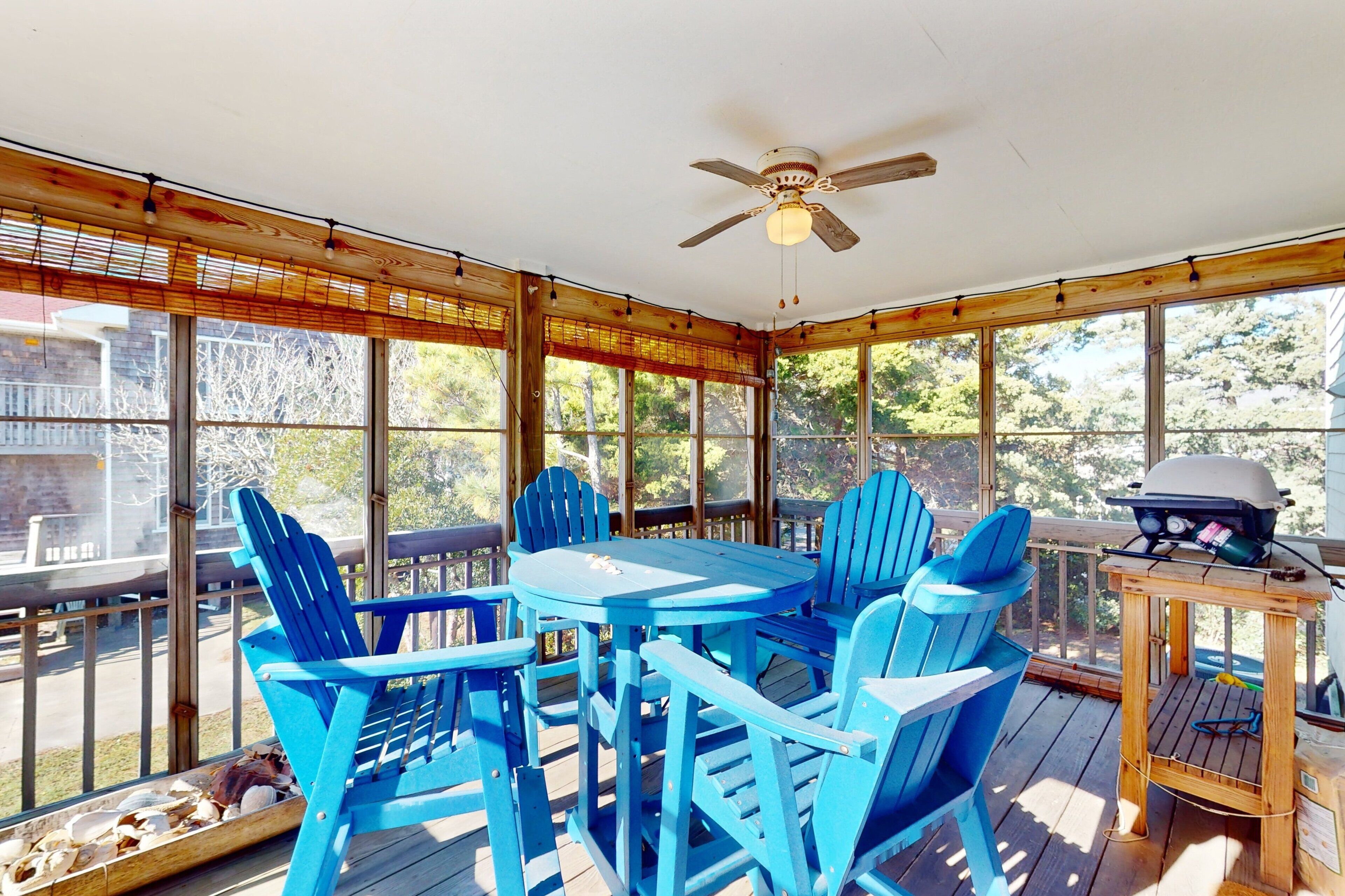 A covered patio with a table and chairs, a ceiling fan, and a grill.