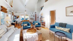 Ein geräumiges Wohnzimmer mit hohen Decken, einem blauen Sofa, einem weißen Sofa und einem Essbereich mit Tisch und Stühlen.