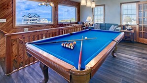 A pool table with balls, a blue pool table, and a wooden railing. - 3-story Pet friendly home with private outdoor pool, hot tub, pool table, & elevator (Waves)