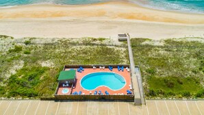 Vista aérea de uma piscina à beira-mar com um deck, rodeada por praia e oceano.