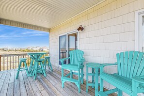 A covered outdoor deck with wooden flooring, a table, and two chairs. - Ocean & Sound Views Await – Just 100 Yards to the Beach with Elevator & Expansive Decks (North Topsail Beach)