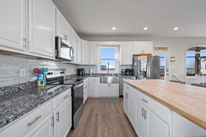 A modern kitchen with white cabinets, granite countertops, stainless steel appliances, and a large window providing a view. - Secluded, updated, dog-friendly beach house with 360-water views, balconies & AC (North Topsail Beach)