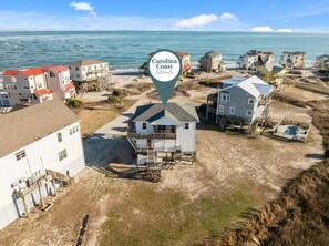 An aerial view of a coastal area with multiple buildings, including a prominent white house with a balcony and a pool area. - Secluded, updated, dog-friendly beach house with 360-water views, balconies & AC (North Topsail Beach)