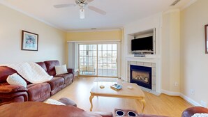 A living room with a brown leather sofa, a wooden coffee table, a fireplace, and a television. - Mystic Marina B: Spacious condo with marina & Intercoastal views, screened-in balconies, W/D & AC (Southport)