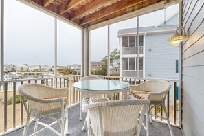 A covered balcony with wicker chairs and a glass table, overlooking a marina and residential buildings.
