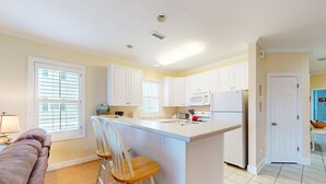 A modern kitchen with white cabinets, a central island, and a dining area with a bench and chairs. - Mystic Marina B: Spacious condo with marina & Intercoastal views, screened-in balconies, W/D & AC (Southport)