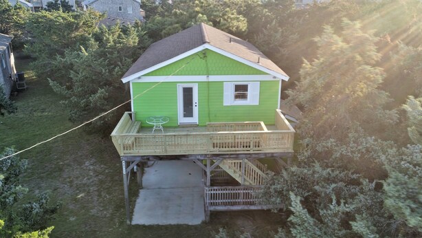 A green house with a wooden deck and a small outdoor seating area.