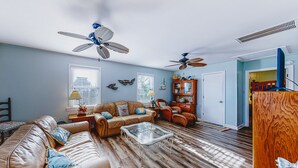 A living room with a brown leather sofa, a glass coffee table, two ceiling fans, a wooden cabinet, and a door leading to another room.