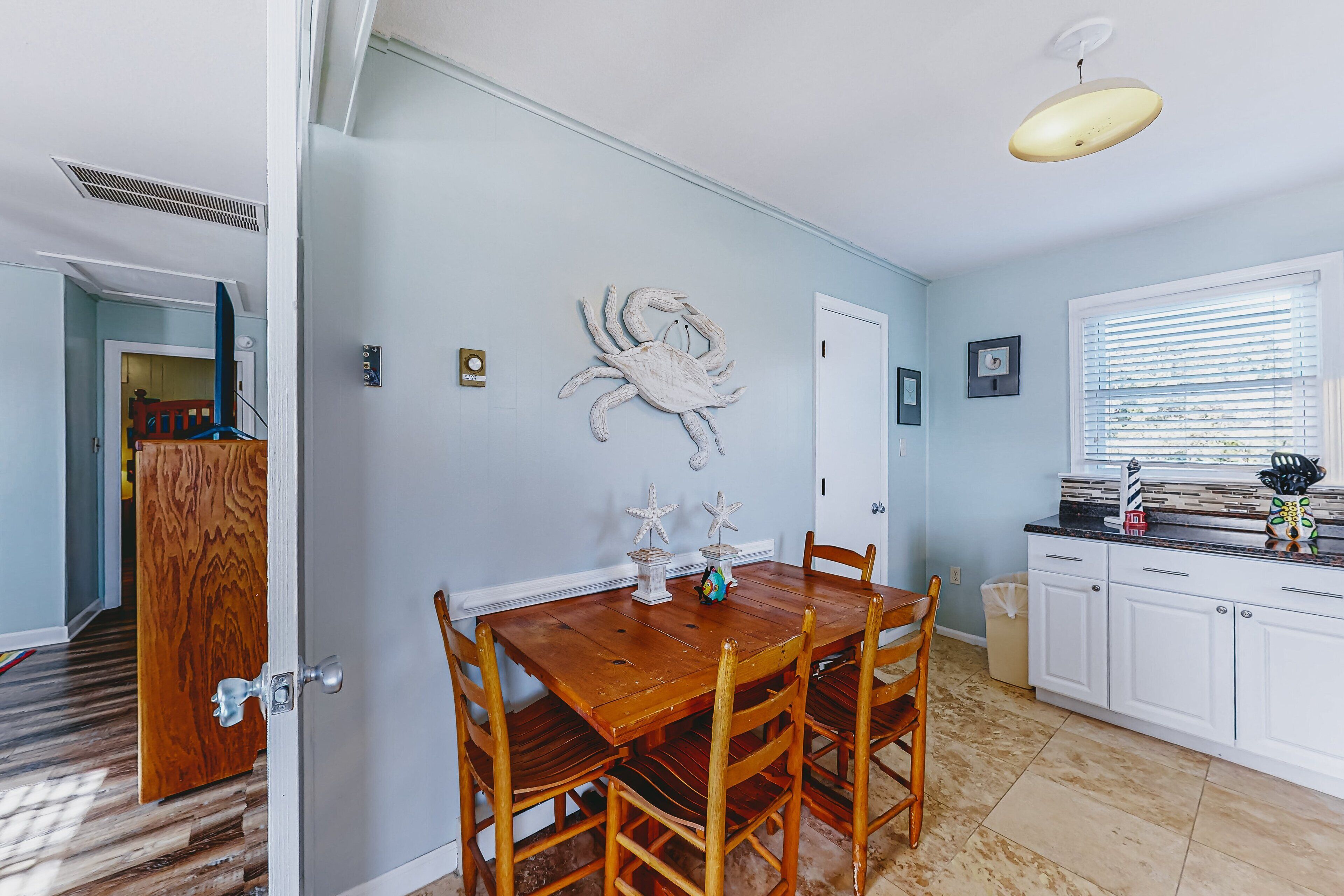 A dining area with a wooden table and chairs, a wall-mounted crab decoration, and a window with blinds.