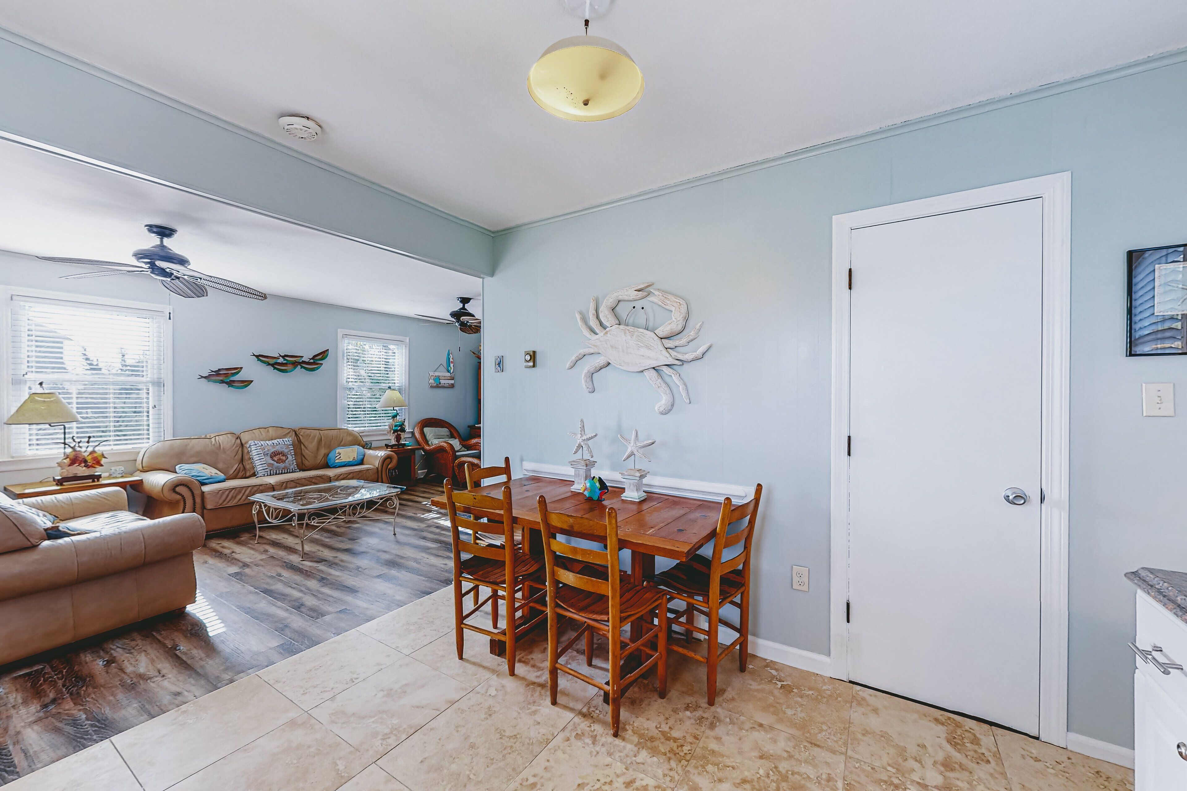 A living room with a wooden dining table, beige sofa, and a ceiling fan.