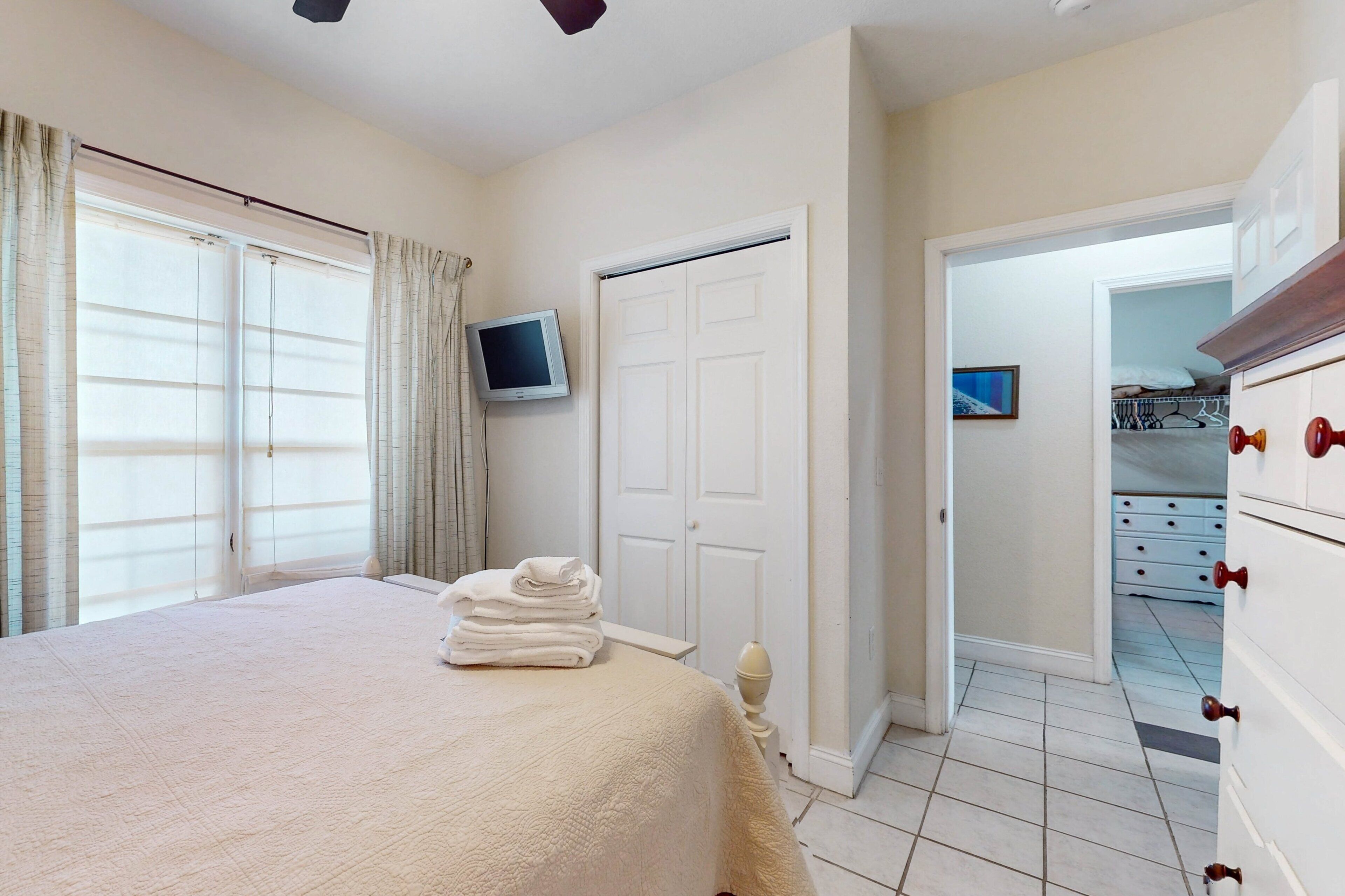 A bedroom with a bed, a TV, a wardrobe, and a door leading to another room.