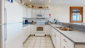 A kitchen with white cabinets, a microwave, an oven, a sink, and a ceiling fan. - First-floor oceanfront home with outdoor pool, hot tub, washer/dryer - dog-friendly (Hatteras)