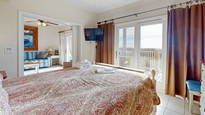 A bedroom with a large bed, a ceiling fan, a TV, a balcony with curtains, and a view of the sea. - First-floor oceanfront home with outdoor pool, hot tub, washer/dryer - dog-friendly (Hatteras)