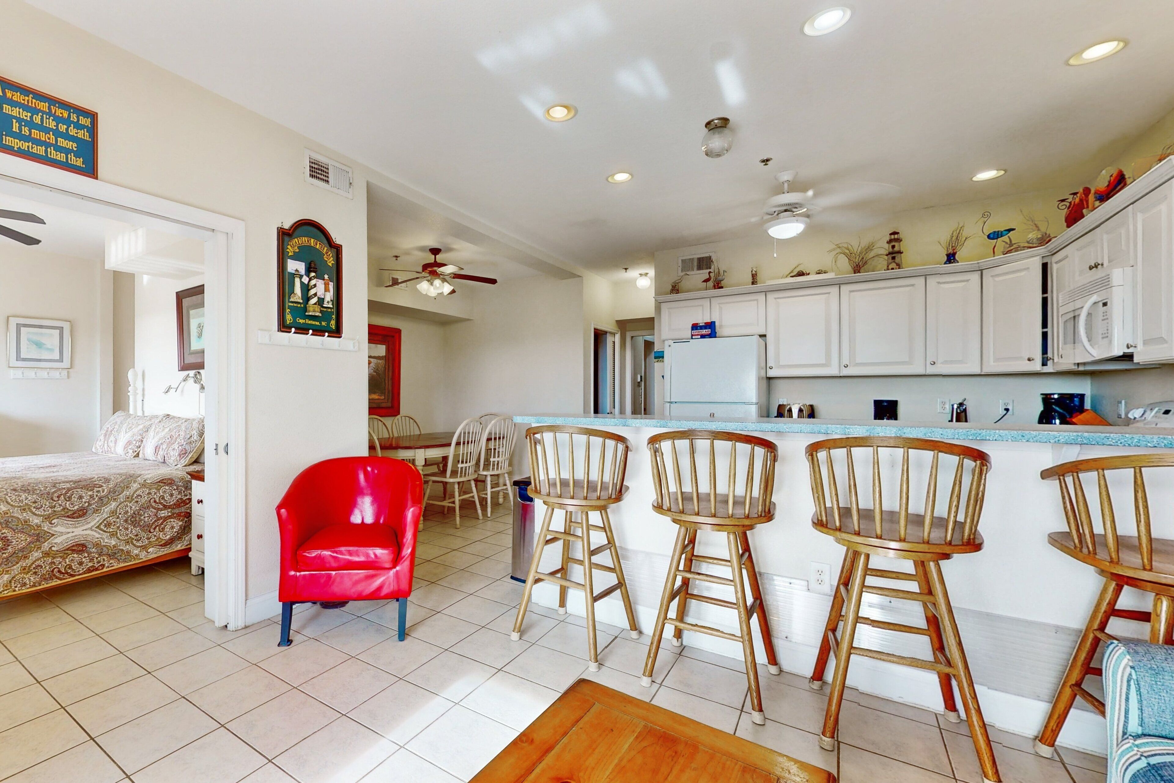 A spacious kitchen with white cabinets, a wooden bar stool area, and a red chair.