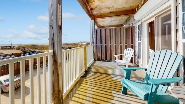 A wooden deck with Adirondack chairs, a view of the beach, and a car parked outside. - First-floor oceanfront home with outdoor pool, hot tub, washer/dryer - dog-friendly (Hatteras)