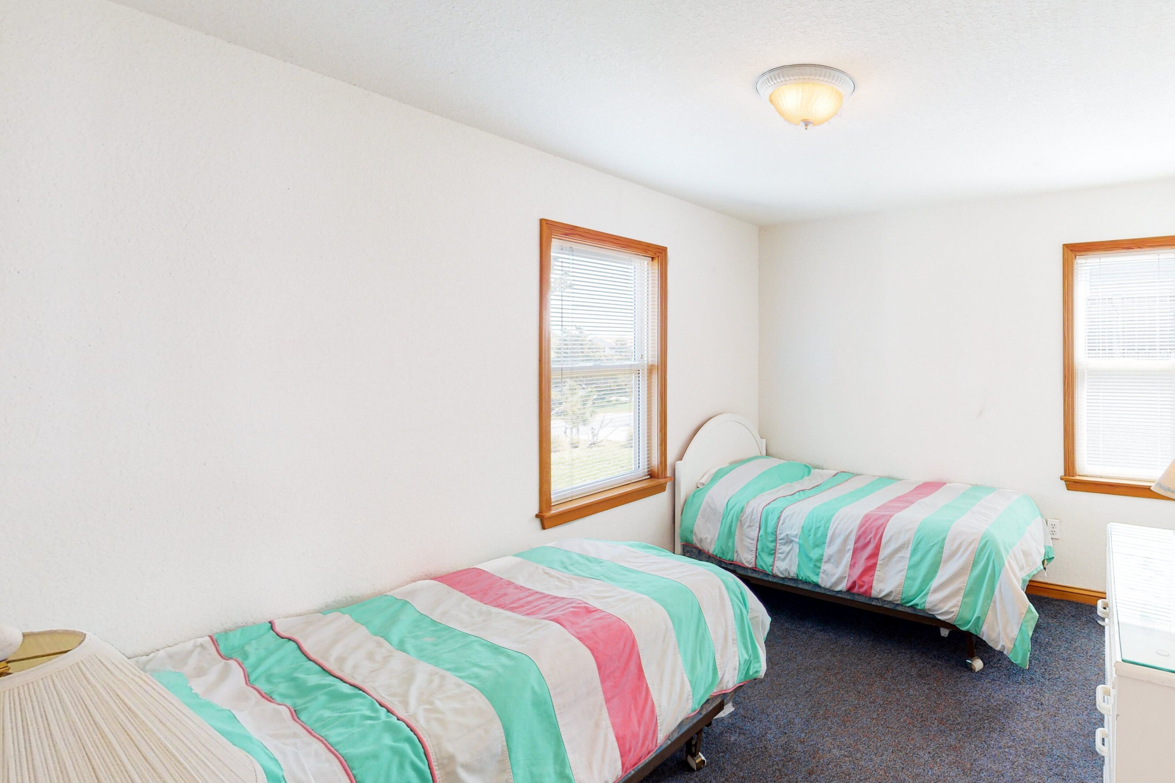 Una habitación con dos camas individuales, cada una con una colcha a rayas, una ventana y una lámpara en el techo.